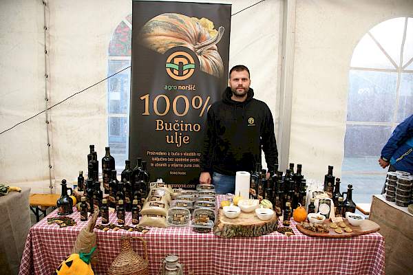 Agro Noršić bučino ulje i sjemenke na drvenom stolu ispred polja bundeva u zalazak sunca.